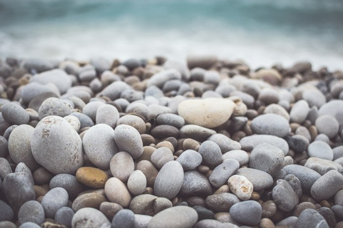 A close up photo of colourful rocks with bokeh effect of the waves in the background
