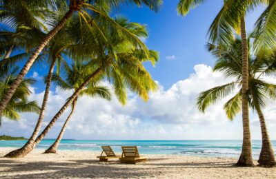 Two beach chairs shaded by palm trees at Half Moon Cay beach.