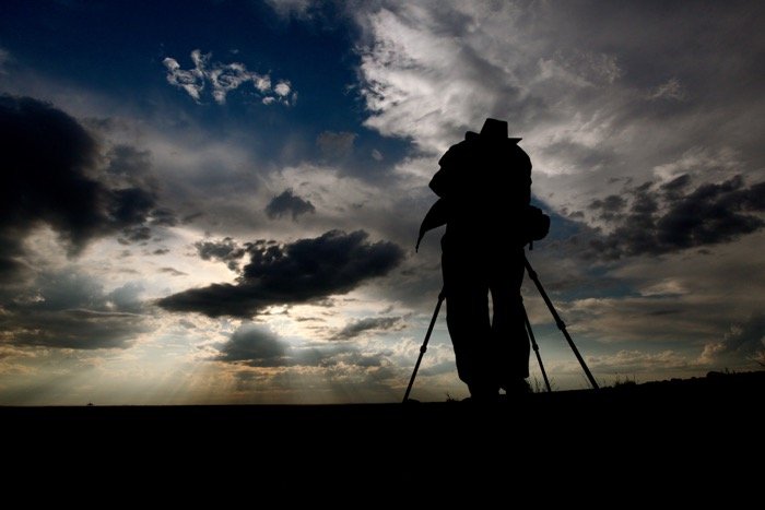 the silhouette of a photographer shooting a landscape on tripod