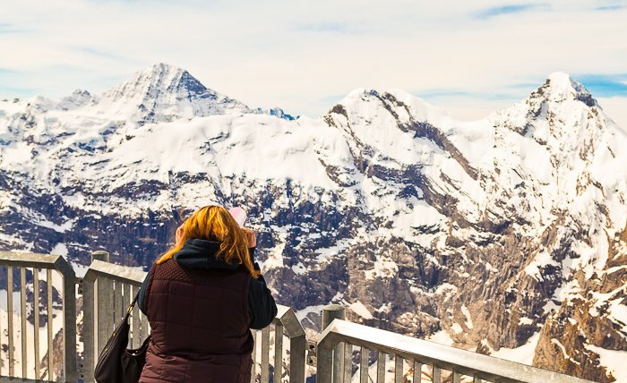 photo of a girl looking from a viewing point at snow capped rocky mountains