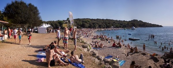 A sandy beach with many people on the sand walking or laying down and some in the water