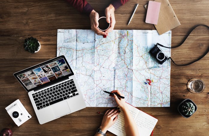 An overhead view of two people making plans for a travel adventure on a wooden table