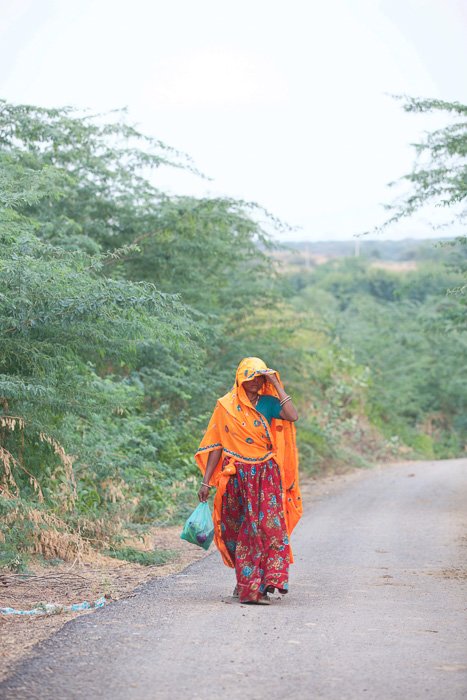 Travel photography of a woman in orange and red clothes walking down a down in India.