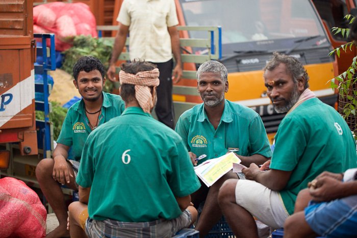 Travel photography of 4 men in green sitting in a flower market in India.