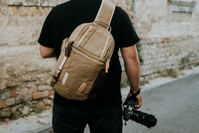 Man with a brown camera bag and a camera in hand walking around an old town