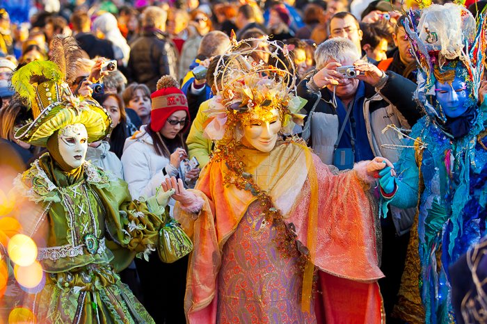 A group of three costumed carnival performers with a crowd behind