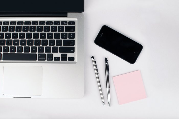 Overhead image of a laptop, smartphone, paper and pens on white desk