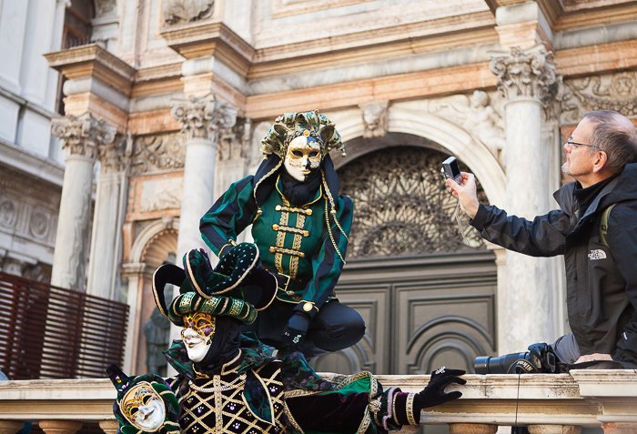 A man holding a camera taking carnival photograph of two performers in green