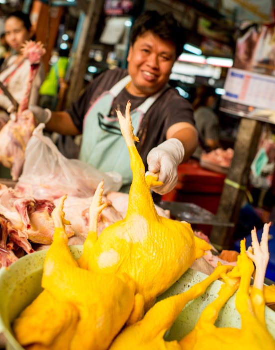 Documentary photography of a butcher in a Thai market pointing to chicken in the foreground