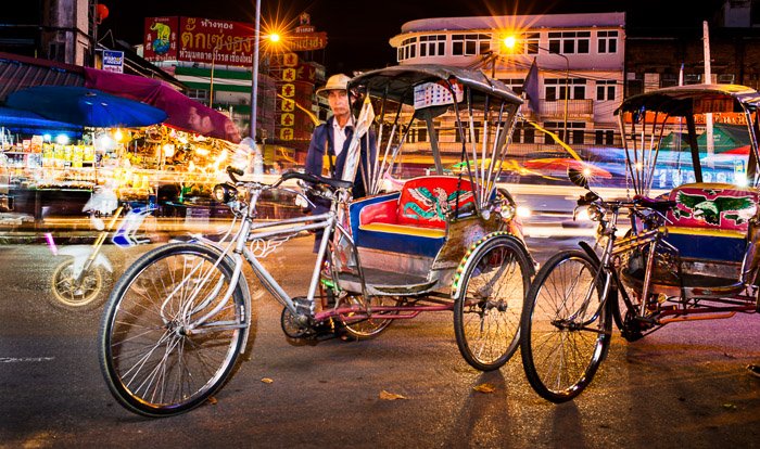 A documentary photography shot of a saamlar driver standing by his vehicle at night