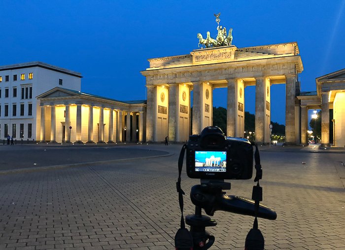 A DSLR camera on a tripod photographing the Brandenburg Gate in Berlin at night