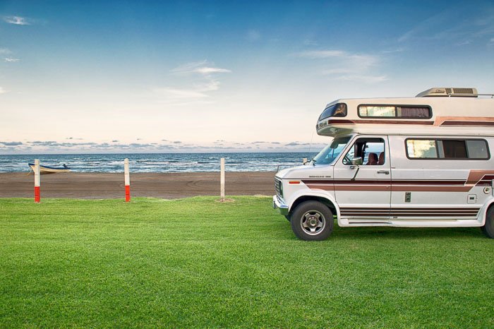 A camper van parked on grass with seascape behind 