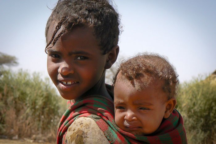 A travel photography shot of a young girl holding a baby on her back - photos of people