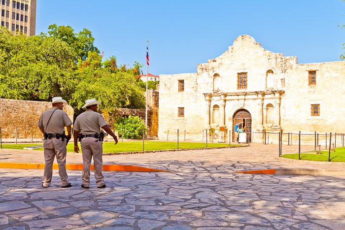 two men looking across a cobblestone street at The Alamo in Texas