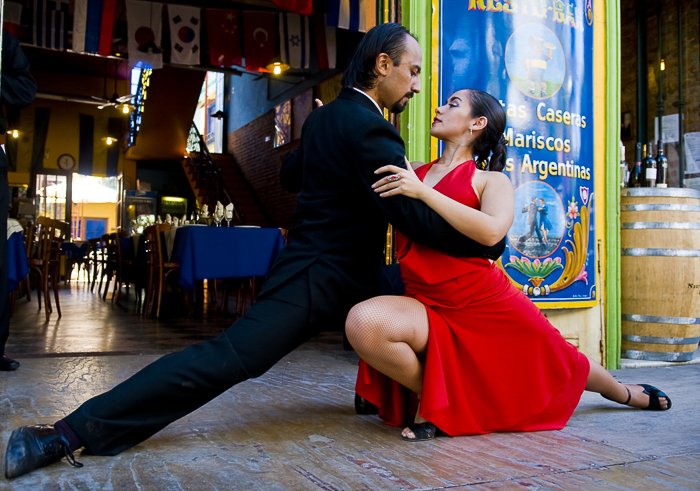 a man and a woman in a red dress looking intensely at each other as they perform a dance