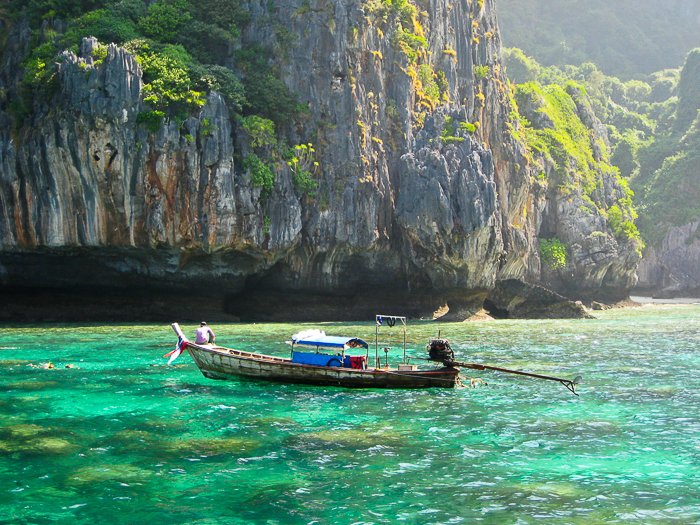 wooden boat on crystal blue green waters in Thailand