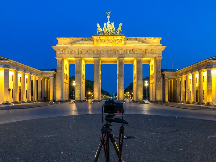 Brandenburg gate at night, lit up by yellow lights, a camera set up on a tripod in front of it - great travel photography destinations