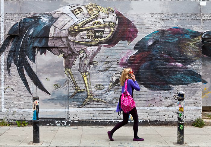 blonde girl in a pink scarf, talking on the phone as she walks past a wall with street art graffiti - travel photography destinations