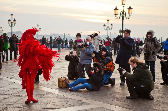 people taking photos of a street performer in a feathery red outfit