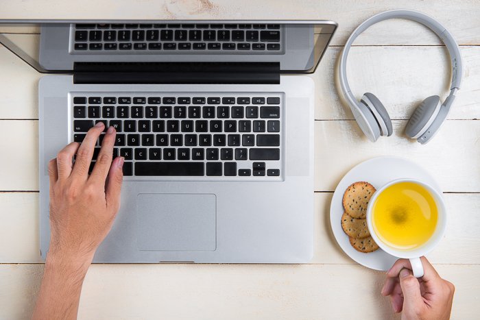 Overhead photo of a person using a laptop and holding a cup of tea.