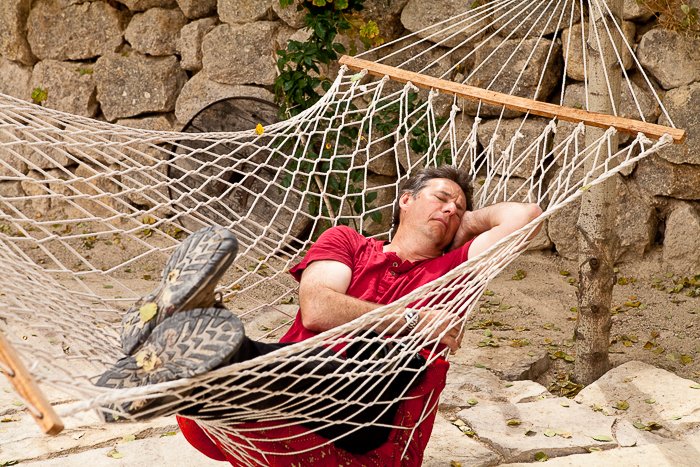 man in a red shirt sleeping in a hammock outdoors, a stone wall in the background - travel safety tips for photographers